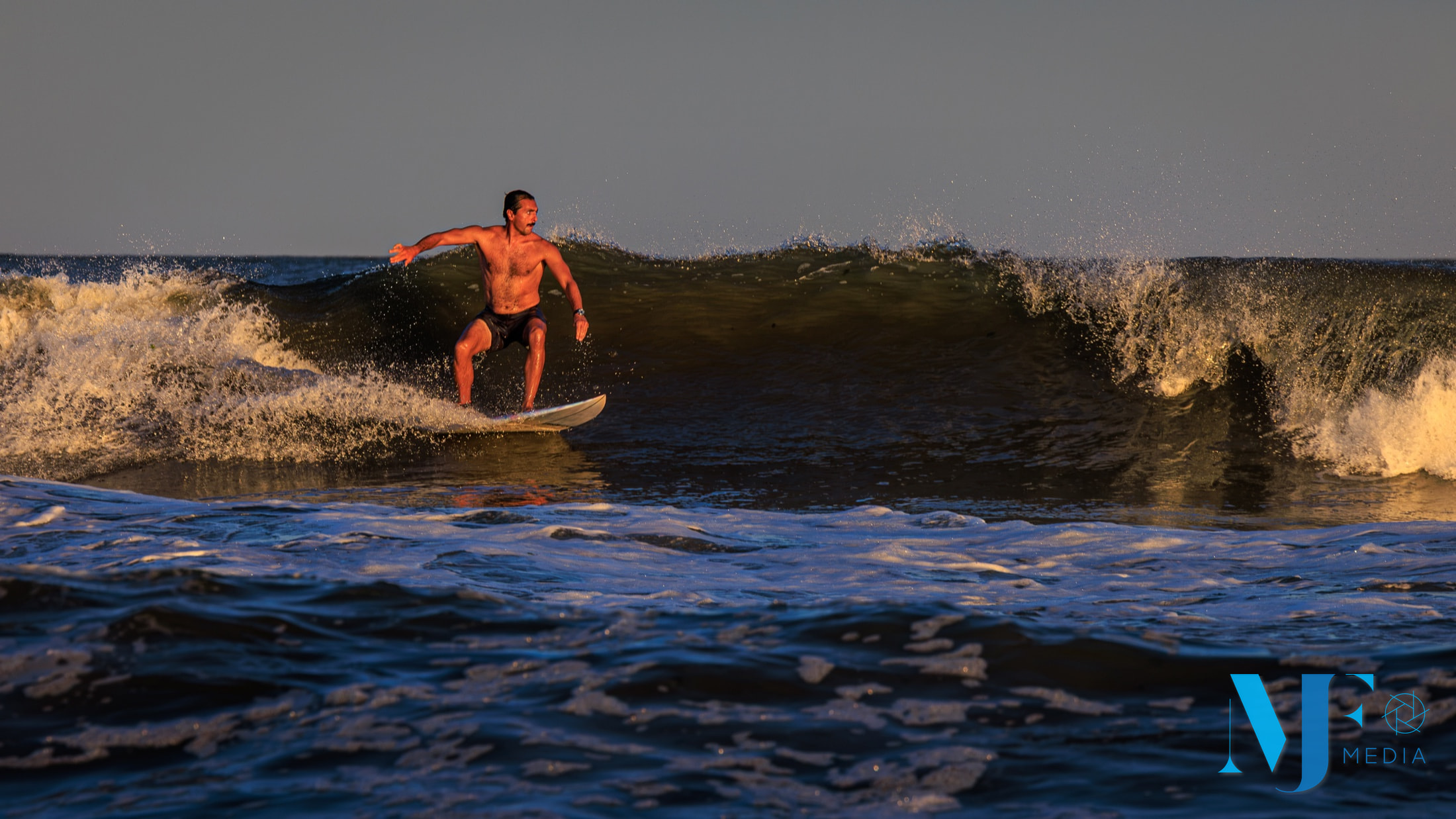 Surfer gliding across a dark wave in warm evening light